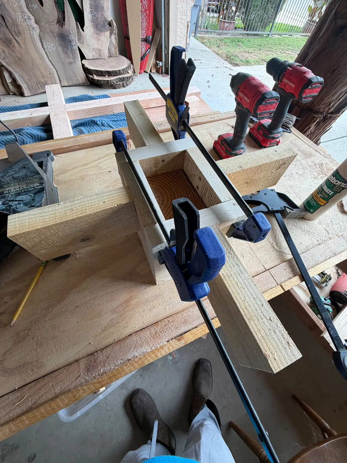 Square wooden socket for the cross base glued and clamped on a workbench with cordless drills nearby
