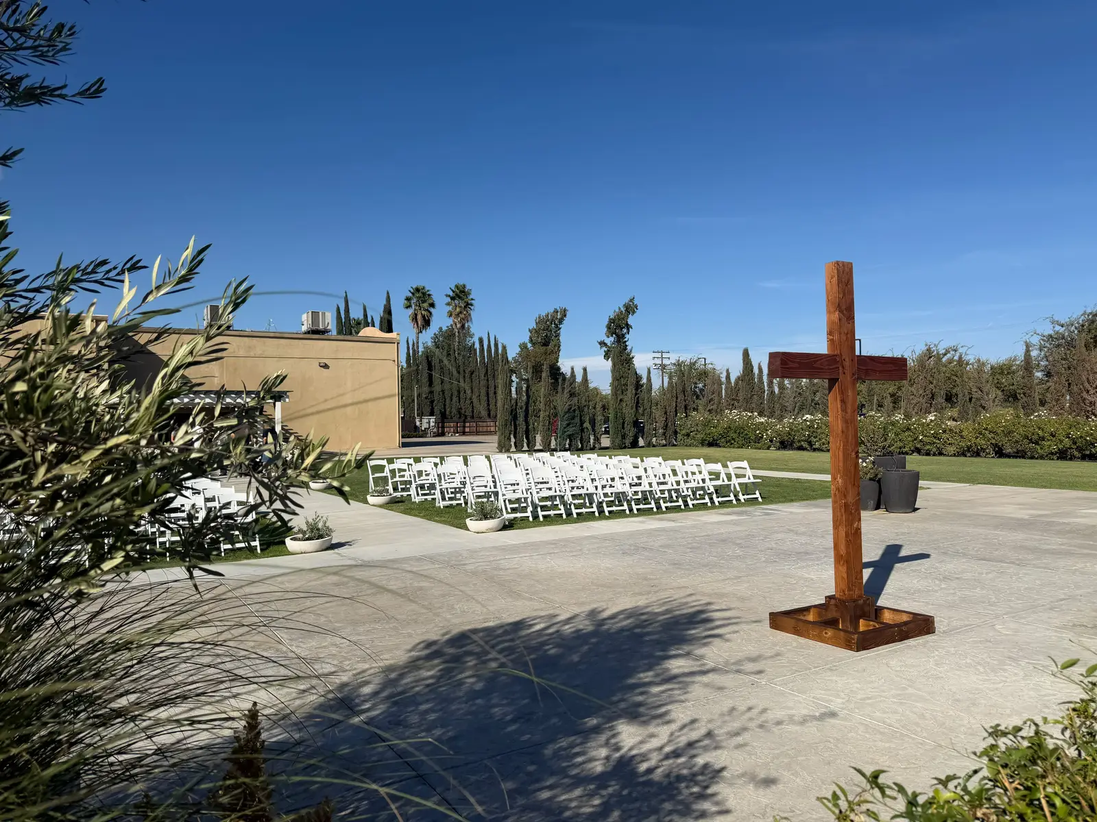 Walnut-stained 7-foot Douglas fir cross standing on a patio near rows of white ceremony chairs